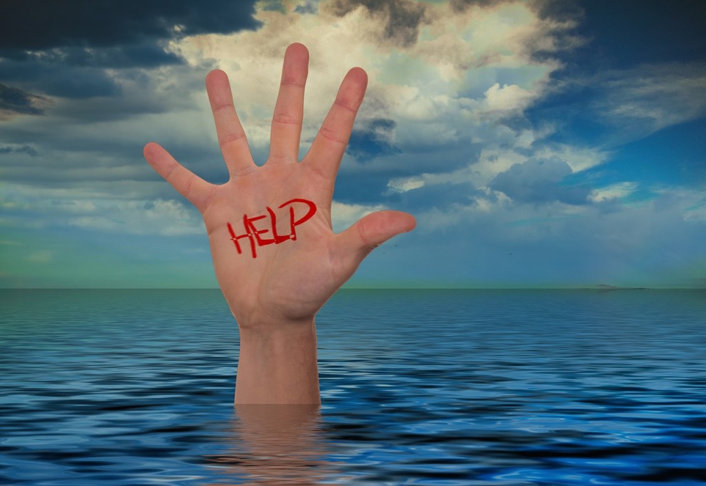 Seascape. Hand waving just above the water suggesting someone drowning - a big red help is painted on the palm of the hand in capital letters.
